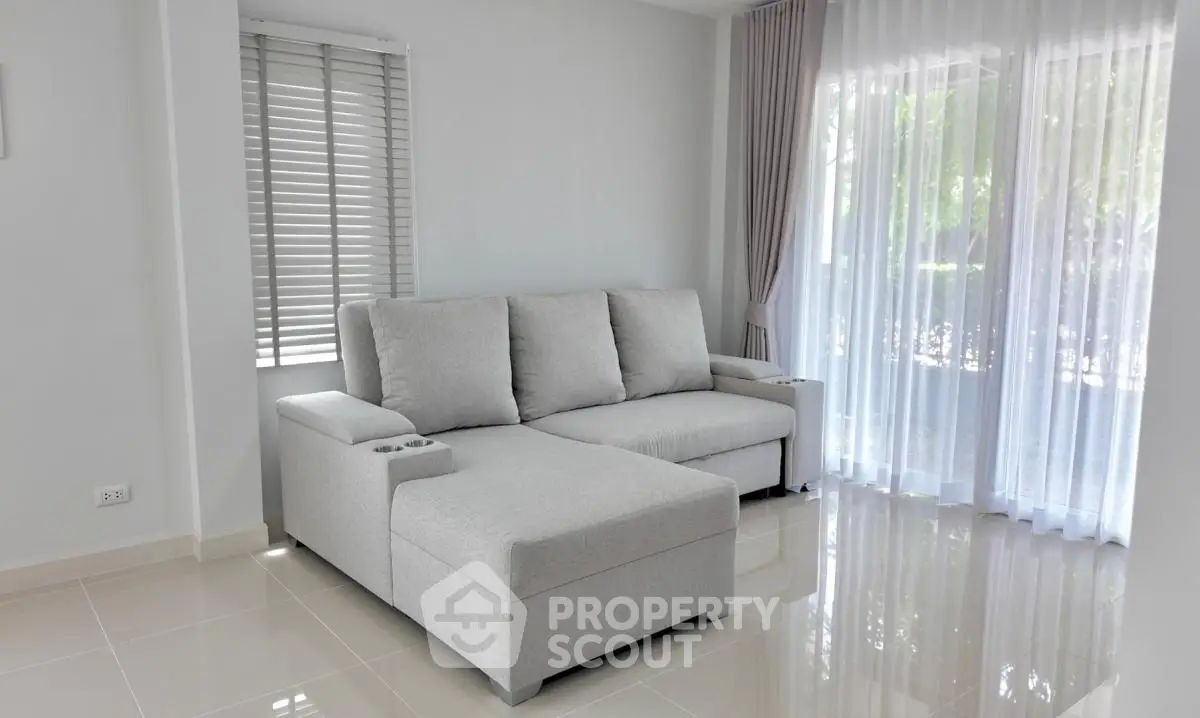 Bright and airy living room with modern gray sectional sofa and large windows with sheer curtains.