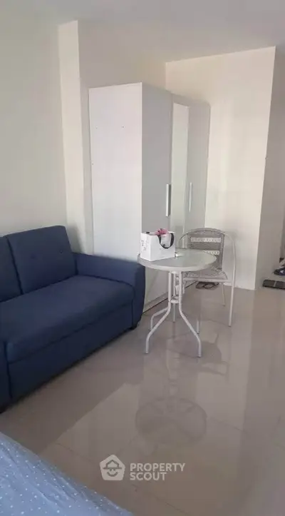 Cozy living room with blue sofa, white wardrobe, and small dining table in modern apartment.