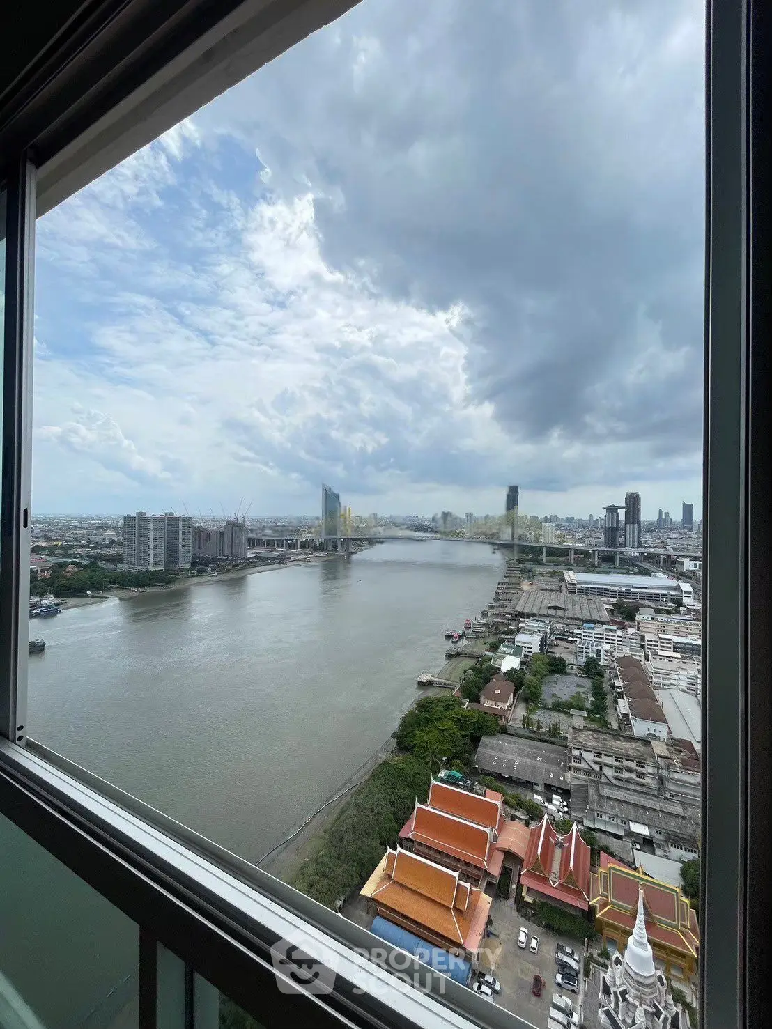 Stunning river view from high-rise apartment window with cityscape and cloudy sky.
