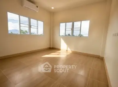 Spacious sunlit room with large windows and wooden flooring, perfect for a cozy living space.