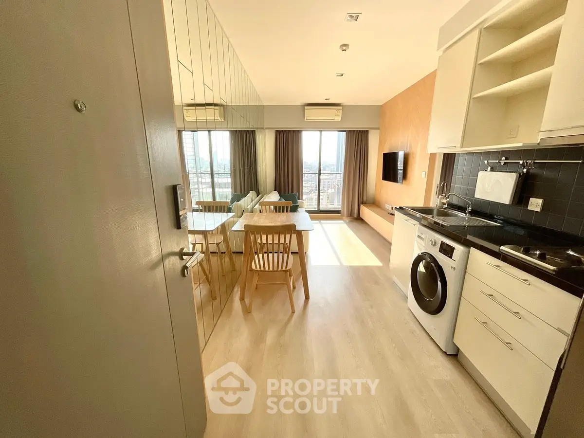 Modern open-plan living room with kitchen and dining area, featuring large windows and stylish decor.