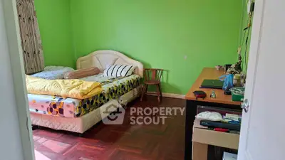 Cozy bedroom with vibrant green walls and parquet flooring, featuring a comfortable bed and a functional workspace.