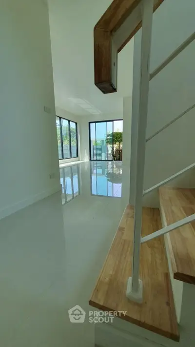 Spacious modern interior with large windows and wooden staircase, perfect for natural light lovers.