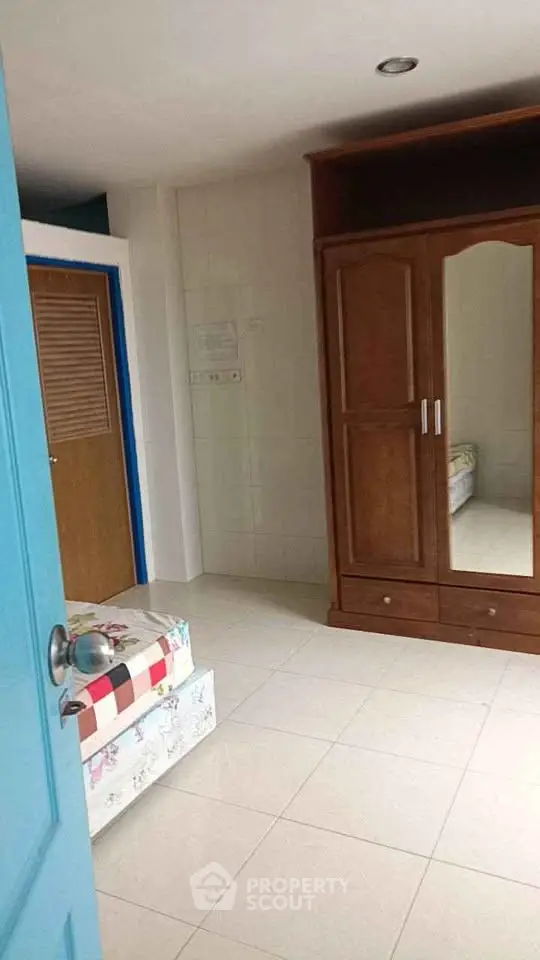 Cozy bedroom with wooden wardrobe and tiled flooring, perfect for comfortable living.