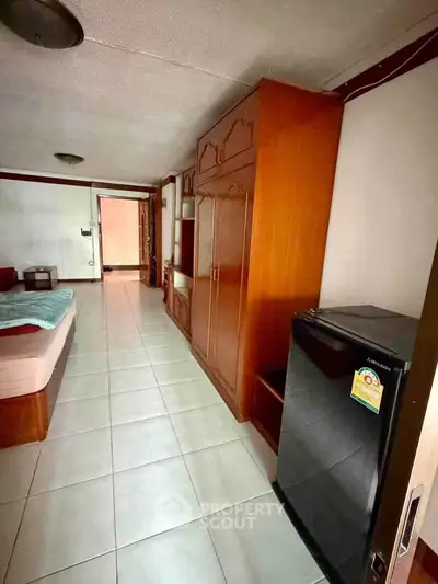 Spacious bedroom with wooden wardrobe and compact refrigerator in cozy apartment.