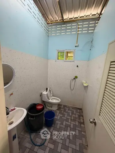 Compact bathroom with high ceiling and basic amenities, featuring a toilet, sink, and shower area.