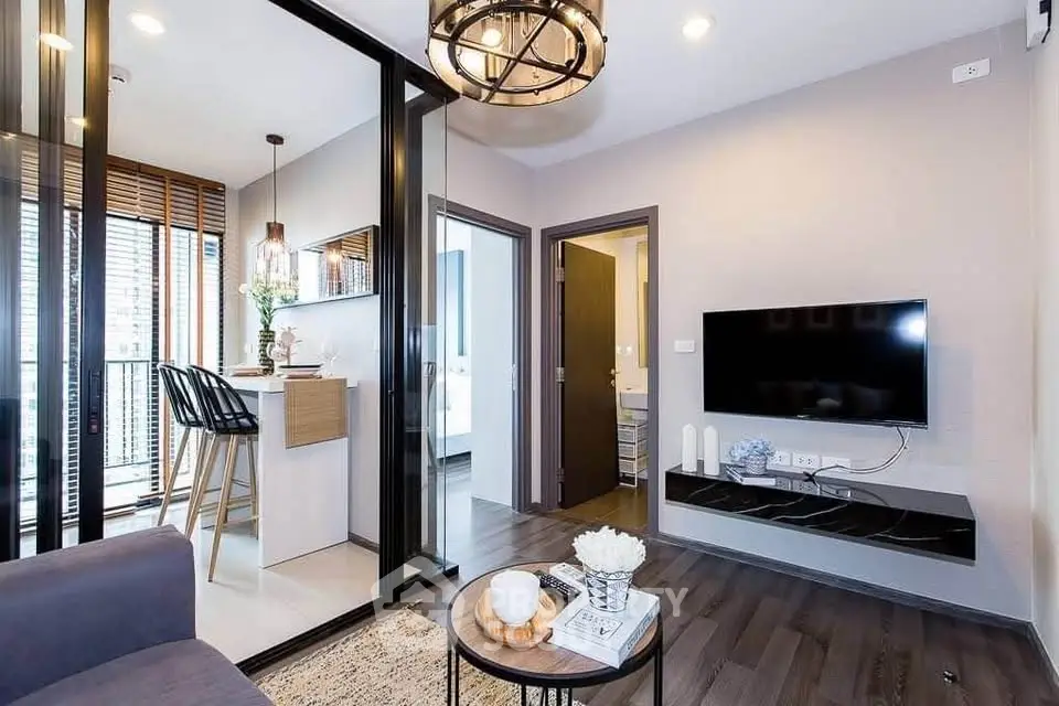 Modern living room with stylish decor and open kitchen layout, featuring a sleek TV setup and elegant lighting.
