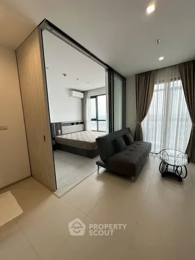 Modern bedroom with sliding doors and cozy seating area, featuring floor-to-ceiling windows.