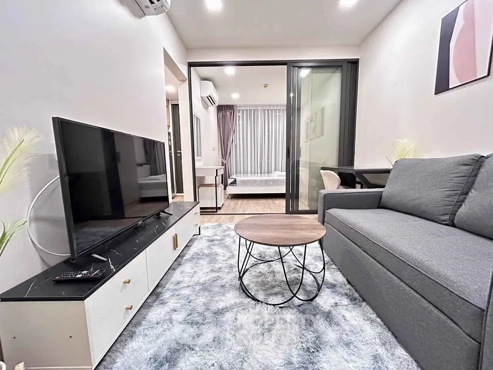 Modern living room with sleek furniture and open layout, featuring a cozy sofa and large TV.