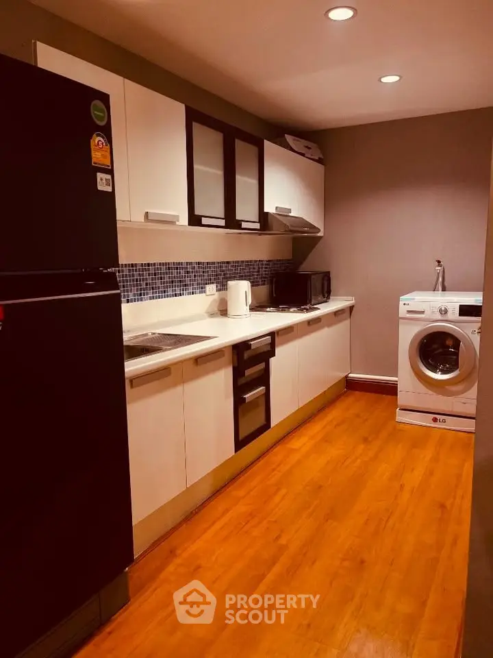 Modern kitchen with sleek appliances and wooden flooring, featuring a washing machine and ample storage.