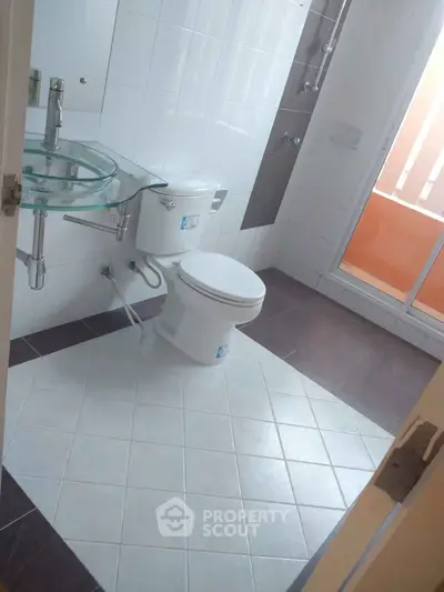 Modern bathroom with glass sink and white tiles, featuring a sleek design and natural light.