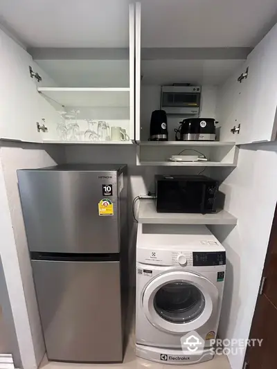 Modern kitchen with fridge, washing machine, microwave, and storage shelves.