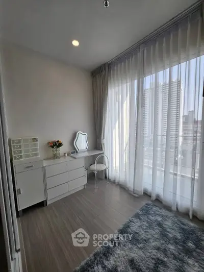 Bright bedroom with modern furniture and large windows offering city views, perfect for urban living.