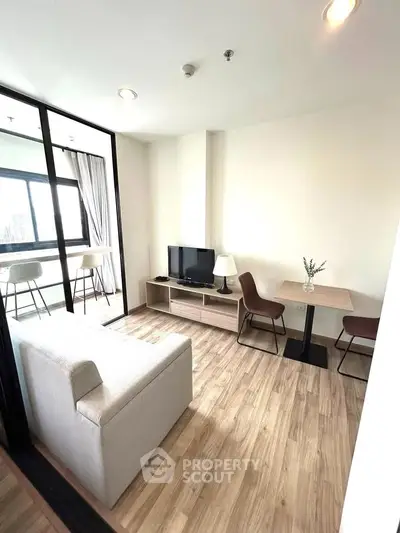 Modern living room with wooden flooring, cozy sofa, TV, and dining area with natural light.