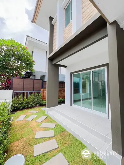 Charming modern home exterior with lush garden and stepping stone path leading to sliding glass doors.