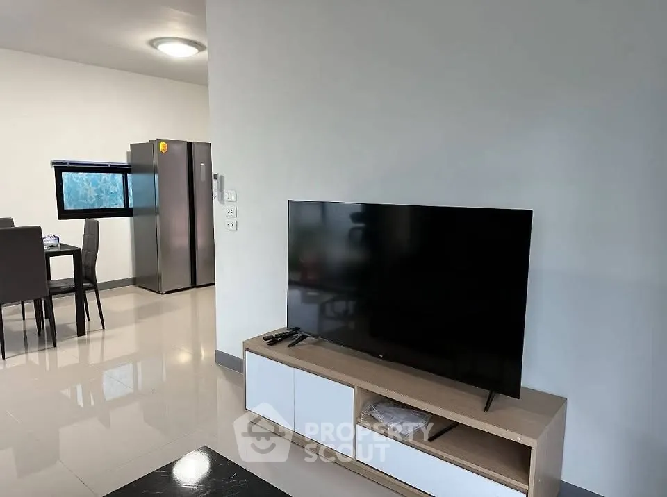 Modern living room with sleek TV and dining area, featuring contemporary furniture and bright lighting.