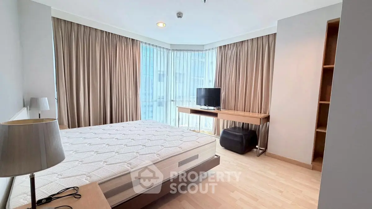 Spacious bedroom with large windows and modern furnishings in a high-rise apartment.