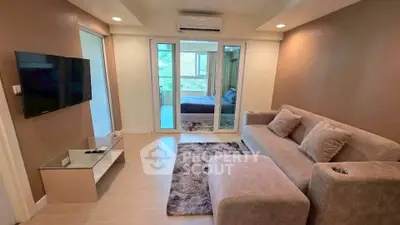 Modern living room with cozy sofa and wall-mounted TV, leading to a bedroom with natural light.