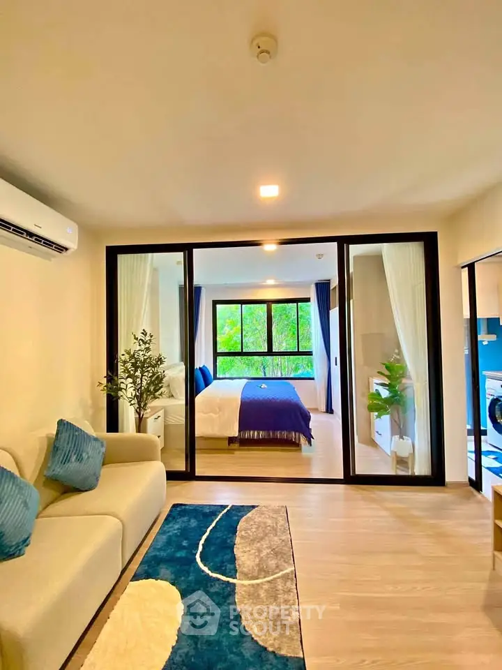 Modern living room with glass doors leading to a bright bedroom, featuring stylish decor and natural light.