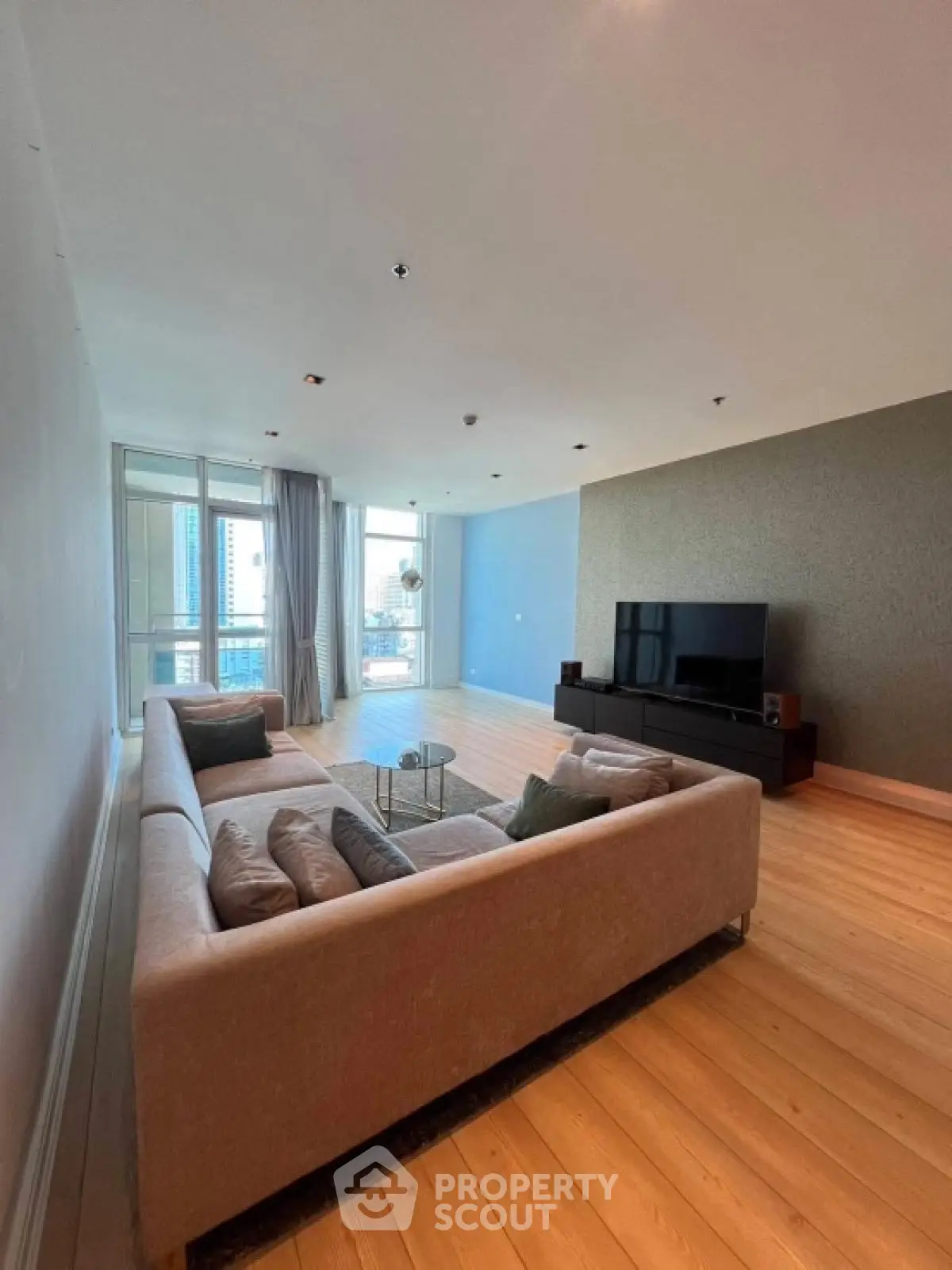 Spacious living room with modern decor and city view, featuring a large sofa and entertainment unit.
