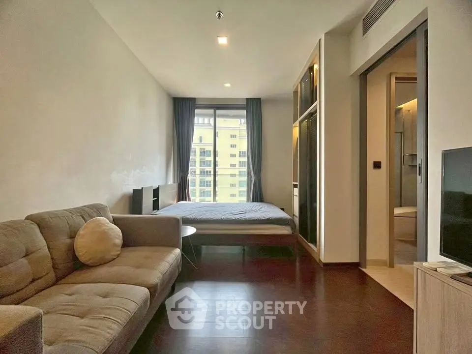 Modern studio apartment with cozy living area and large window view.