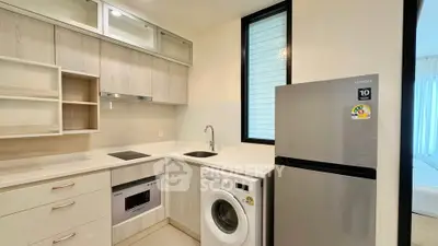 Modern kitchen with sleek appliances including washing machine and fridge, featuring a compact open layout.