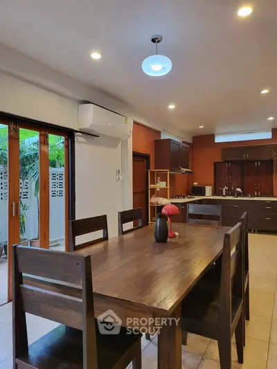 Spacious dining area with wooden table and chairs, adjacent to a modern kitchen with outdoor view.
