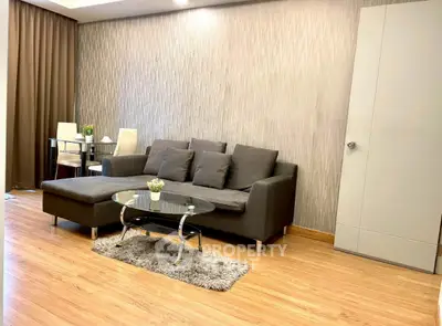 Modern living room with stylish gray sofa and glass coffee table on wooden flooring.