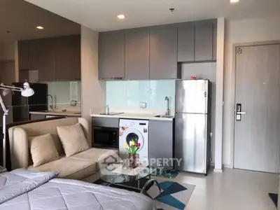 Modern studio apartment with sleek kitchen and cozy living area, featuring a washing machine and stainless steel fridge.