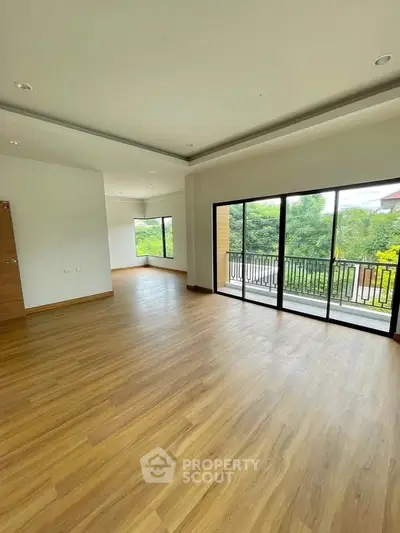 Spacious living room with large windows and balcony access, featuring elegant wooden flooring.