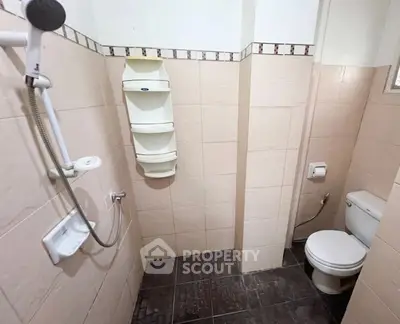 Compact bathroom with shower and toilet, tiled walls and floor, ideal for efficient space use.