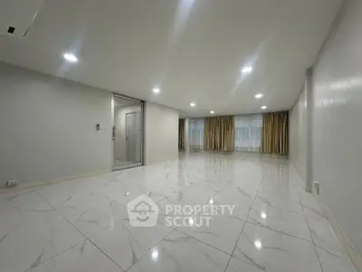 Spacious modern living room with marble flooring and large windows with curtains.