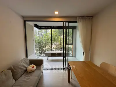 Modern living room with sliding glass doors leading to a lush garden view, featuring cozy sofa and wooden dining table.