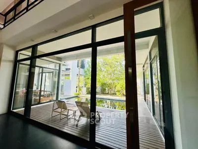 Spacious living area with floor-to-ceiling windows opening to a serene wooden deck and lush greenery, perfect for indoor-outdoor living.