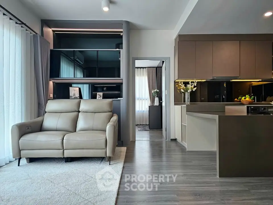 Modern open-layout living room with sleek kitchen and cozy seating area, featuring elegant decor and natural light.
