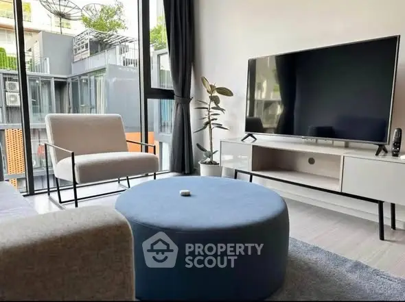 Modern living room with large TV, stylish furniture, and floor-to-ceiling windows offering natural light.