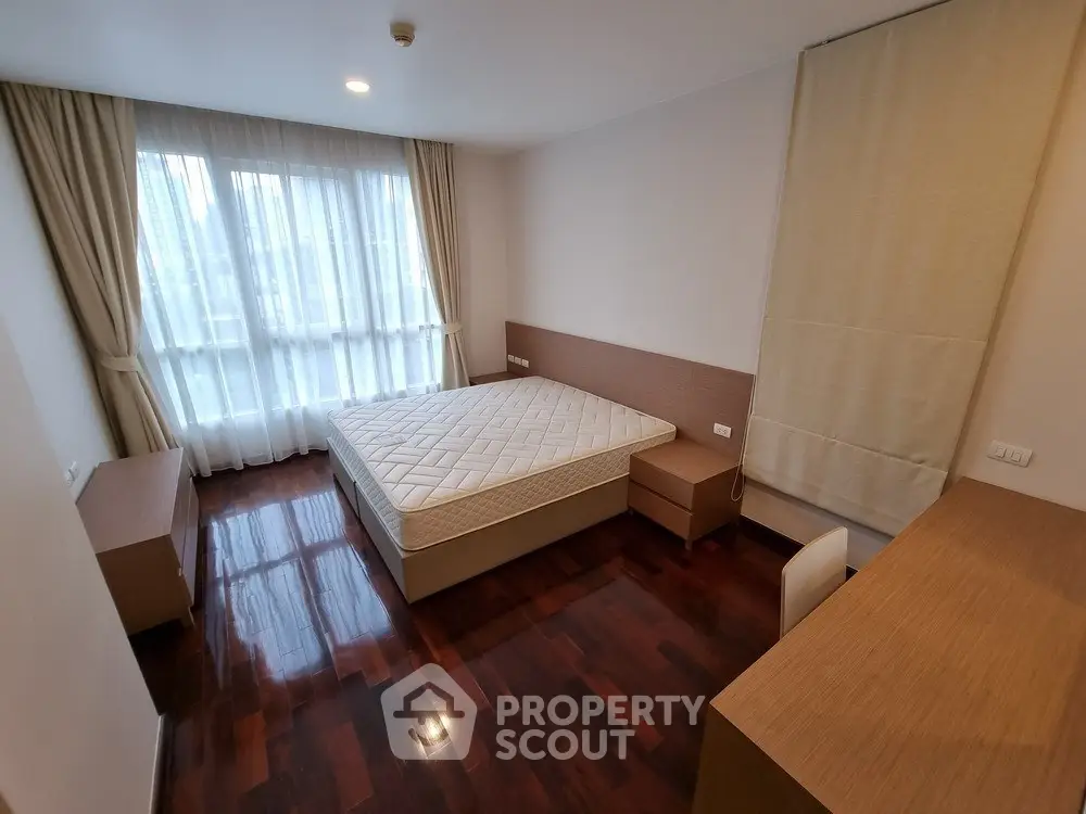 Spacious bedroom with hardwood floors and large window in modern apartment