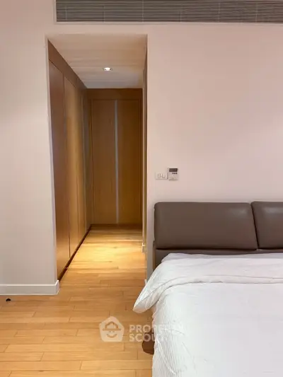 Modern bedroom with sleek wooden flooring and built-in wardrobe, featuring a cozy bed and minimalist design.
