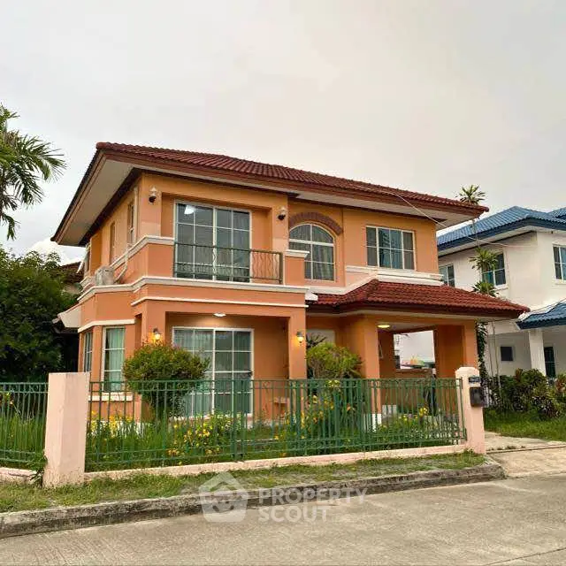 Charming two-story house with red roof and green fence in suburban neighborhood.