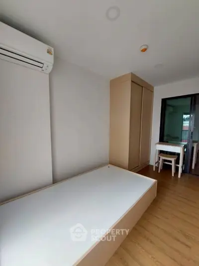 Modern minimalist bedroom with wooden flooring and built-in wardrobe, featuring air conditioning and natural light.