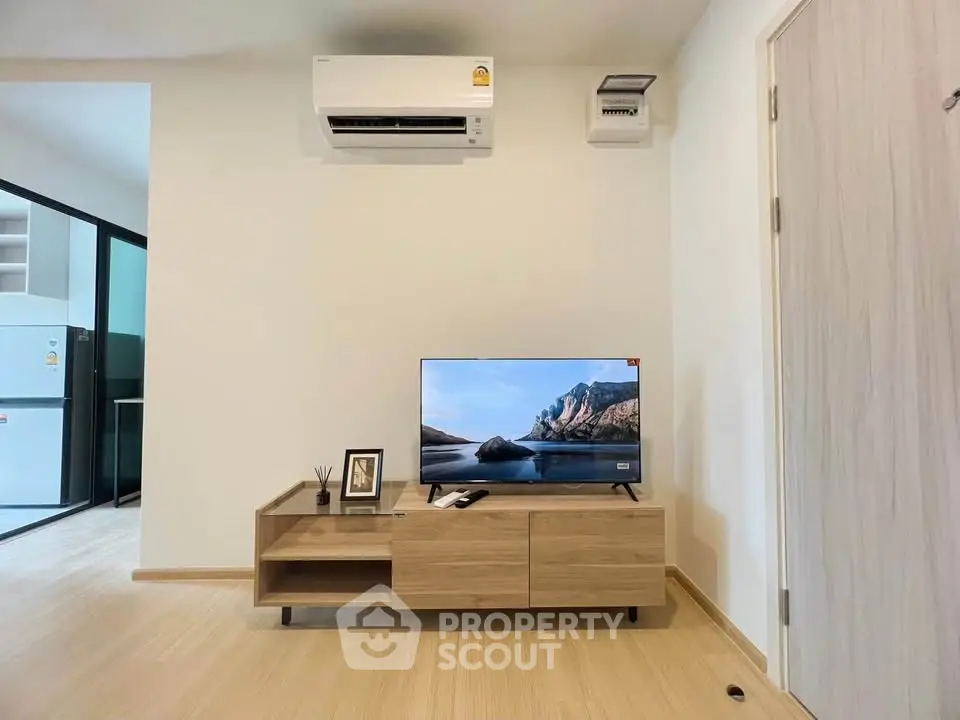 Modern living room with sleek TV stand, air conditioning, and view into a contemporary kitchen.