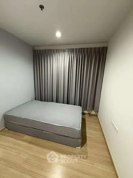 Minimalist bedroom with wooden flooring and large window curtains.