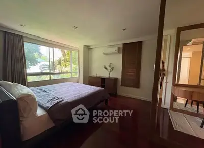 Spacious bedroom with large window and elegant wooden flooring.