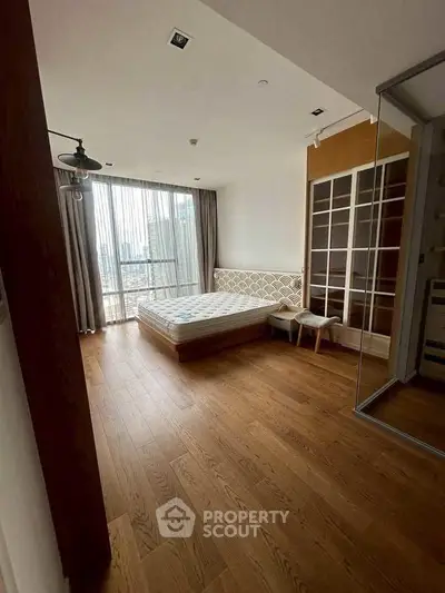 Spacious bedroom with wooden flooring and large window offering city view