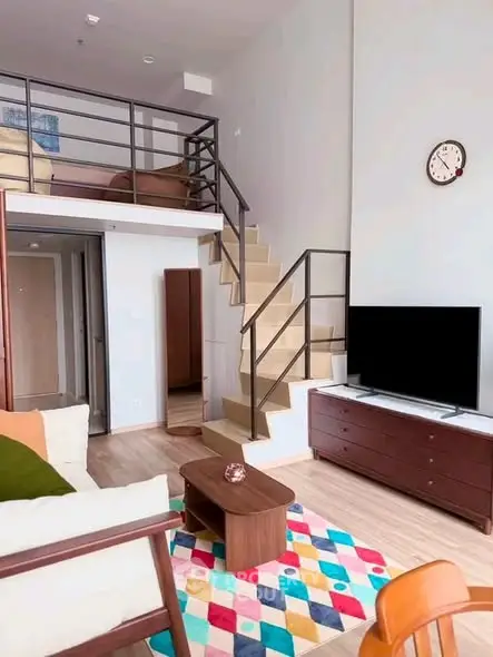 Modern loft-style living room with mezzanine, colorful rug, and sleek furniture.