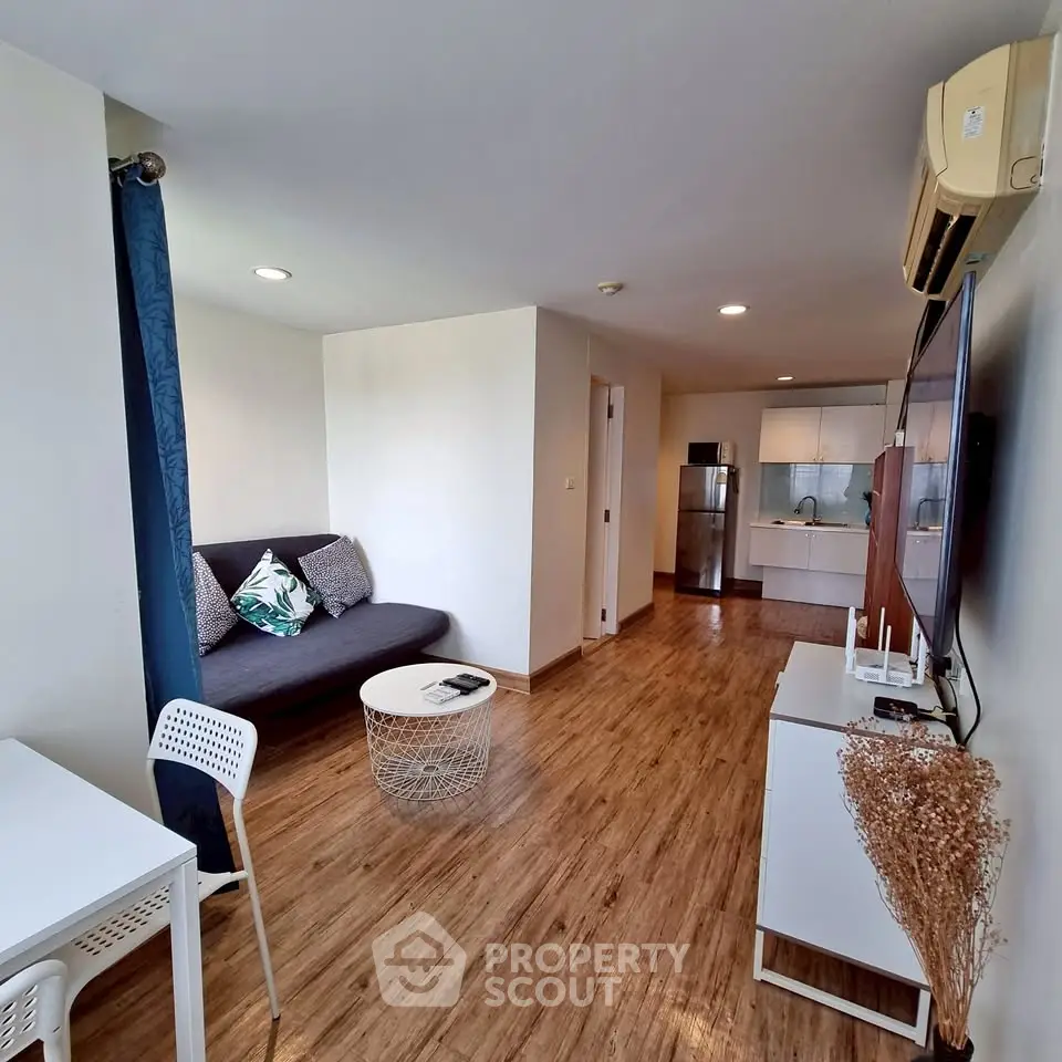 Modern living room with wooden flooring, stylish furniture, and open kitchen layout in a cozy apartment.