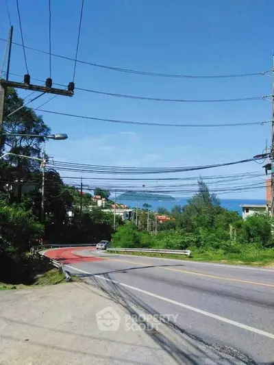 Scenic road view with lush greenery and distant ocean horizon, ideal for serene living.