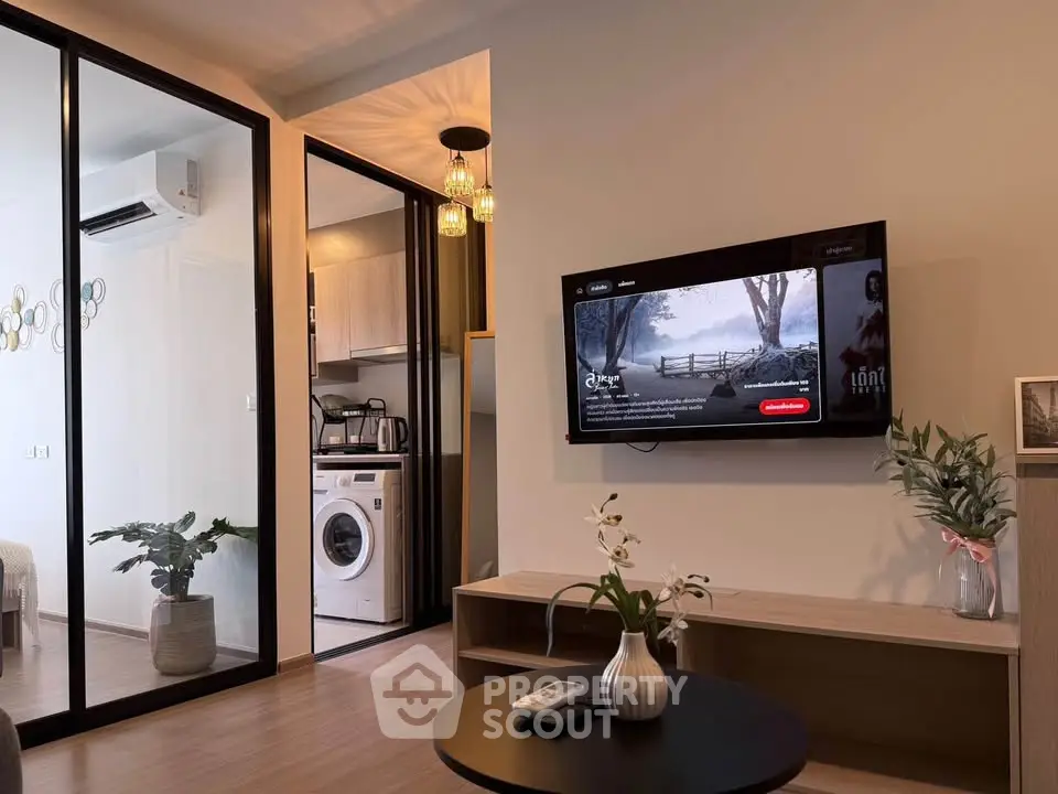 Modern living room with wall-mounted TV and view into kitchen with washing machine.