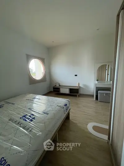 Spacious bedroom with modern design and unique circular window, featuring wooden flooring and stylish furniture.