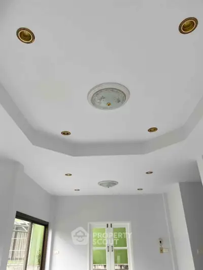 Modern interior with recessed lighting and elegant ceiling design in a bright room with large windows.
